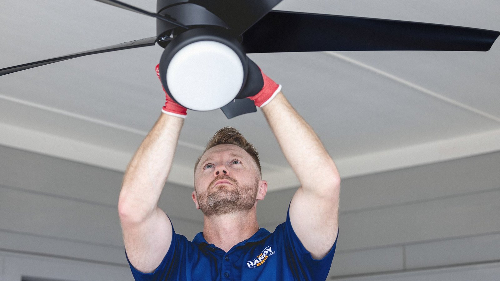 Warren Wiedenfeld of The Handy Bro finishing a black ceiling fan installation, light kit in hand