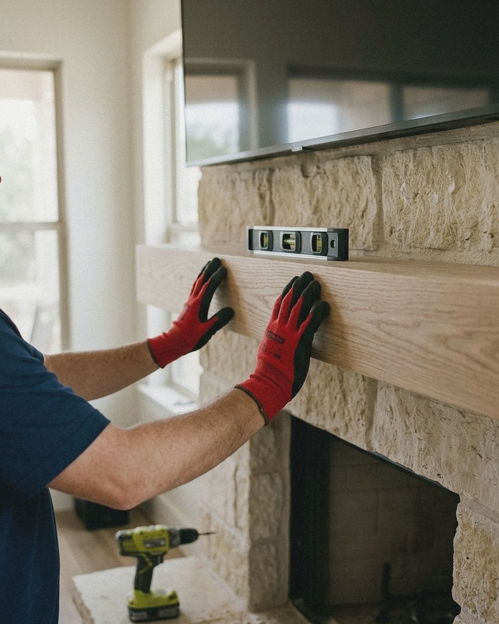 Gloved hands setting a white oak floating mantel shelf on a limestone fireplace
