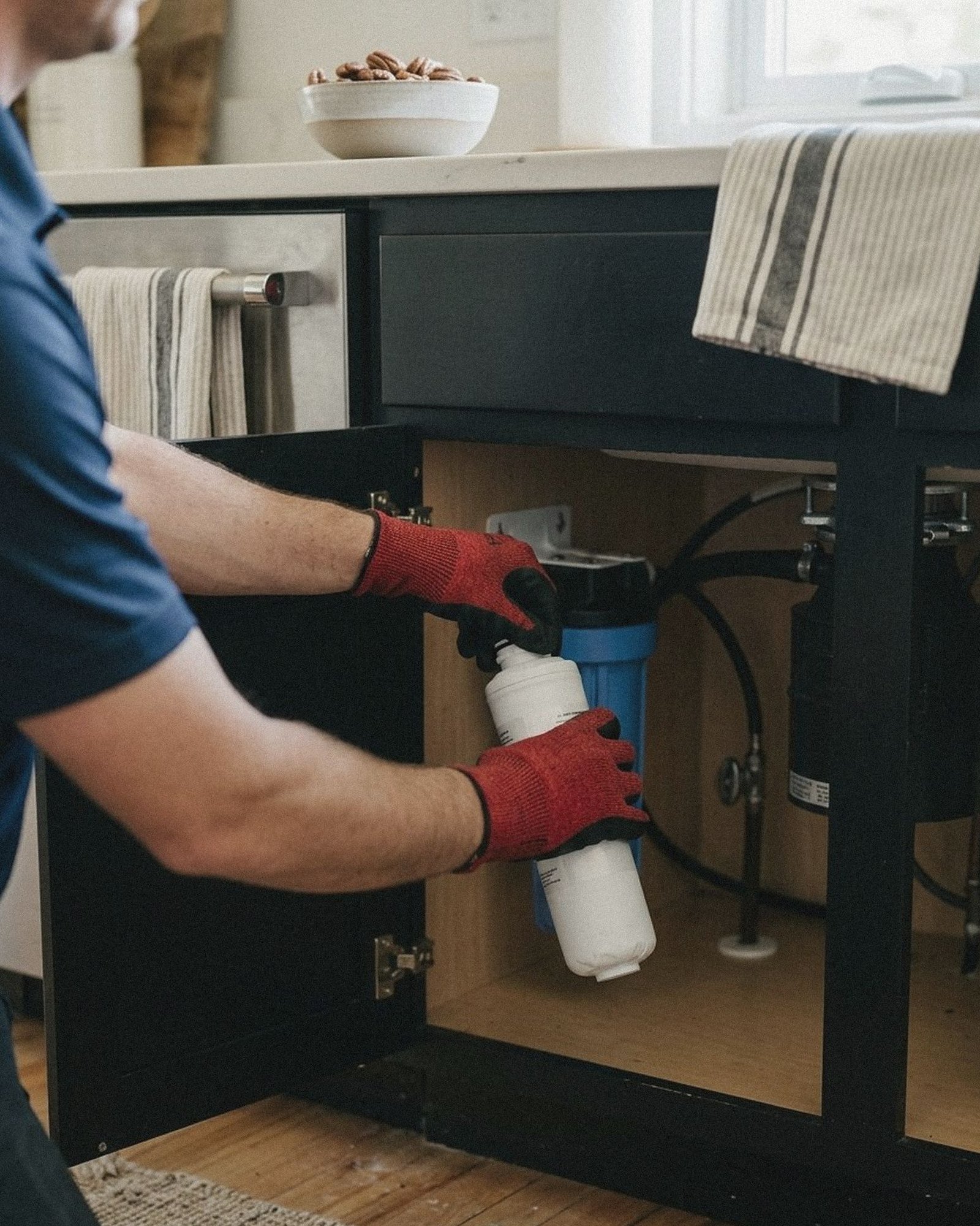 Gloved hands twisting a fresh filter cartridge into an under sink water filtration housing